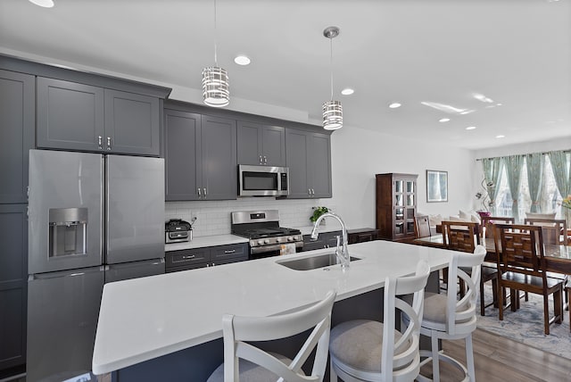 kitchen with appliances with stainless steel finishes, backsplash, a kitchen island with sink, sink, and pendant lighting