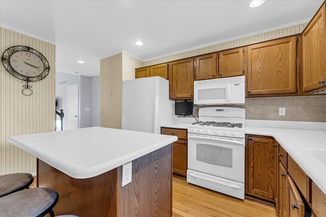 kitchen featuring white appliances, a kitchen breakfast bar, crown molding, light wood-type flooring, and tasteful backsplash