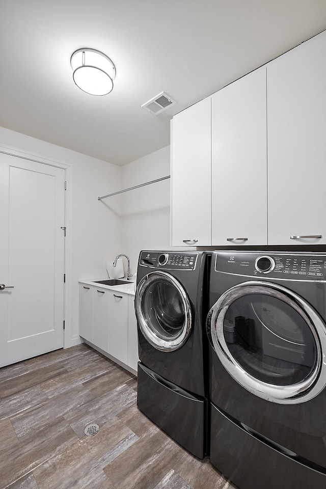 washroom featuring separate washer and dryer, cabinet space, and wood finished floors