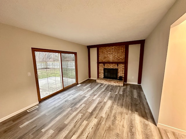 unfurnished living room with hardwood / wood-style flooring, a textured ceiling, and a brick fireplace