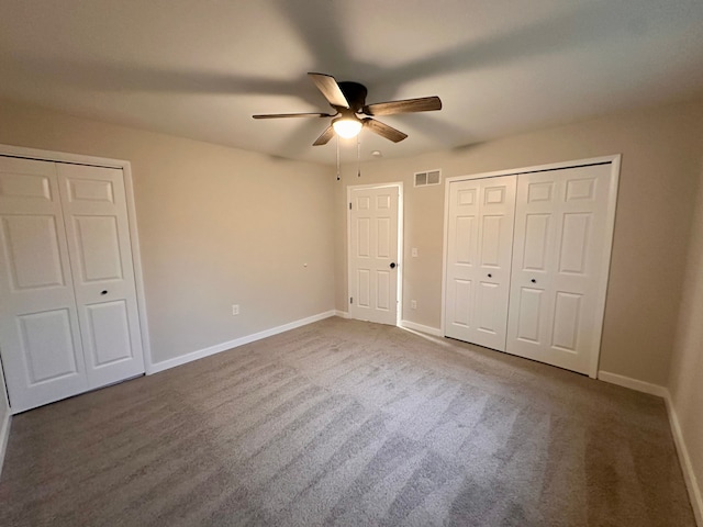 unfurnished bedroom with two closets, dark carpet, and ceiling fan