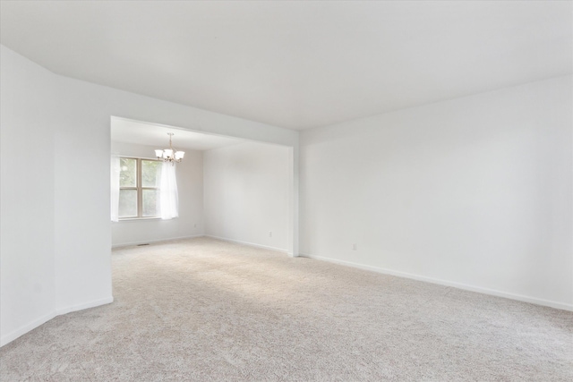 empty room with light carpet and a notable chandelier