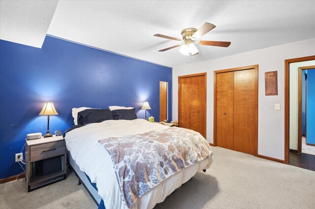 bedroom with light carpet, a textured ceiling, ceiling fan, and multiple closets