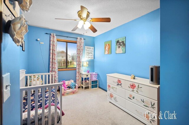 bedroom with a crib, a textured ceiling, ceiling fan, and carpet flooring