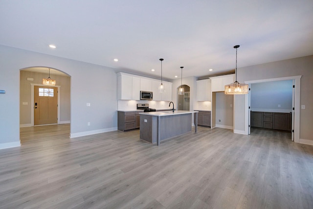 kitchen featuring appliances with stainless steel finishes, sink, a center island with sink, white cabinets, and hanging light fixtures