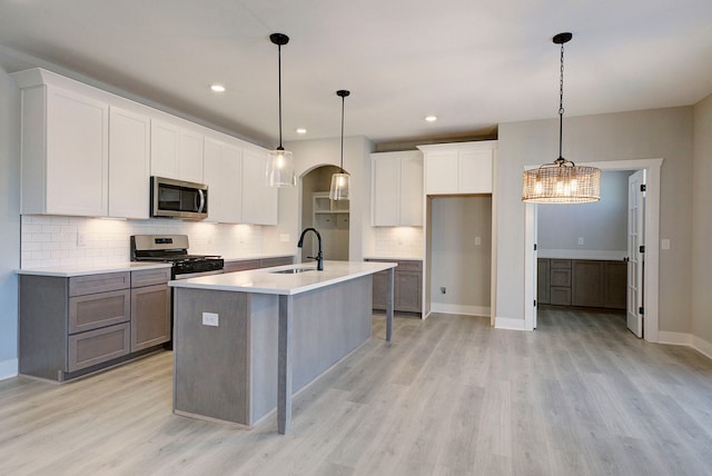 kitchen with white cabinets, appliances with stainless steel finishes, a kitchen island with sink, and hanging light fixtures