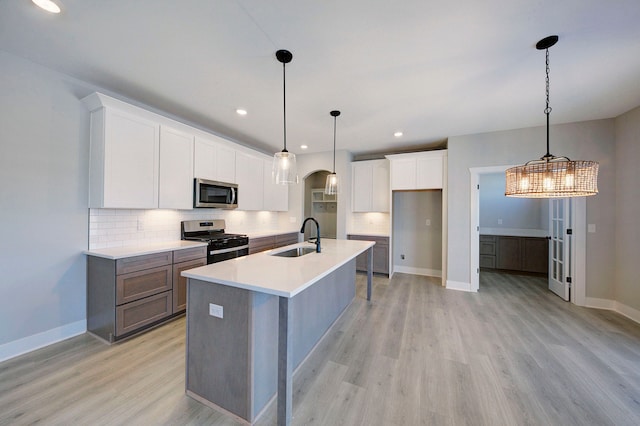 kitchen with sink, stainless steel appliances, pendant lighting, a kitchen island with sink, and white cabinets