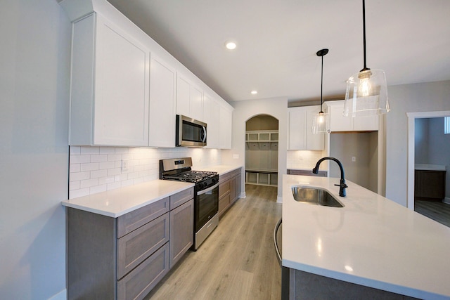 kitchen featuring light wood-type flooring, stainless steel appliances, sink, pendant lighting, and white cabinets