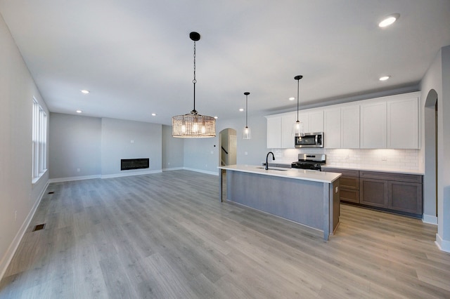 kitchen with appliances with stainless steel finishes, sink, decorative light fixtures, white cabinets, and an island with sink