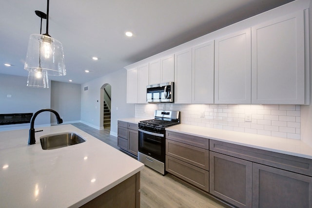 kitchen featuring white cabinetry, sink, hanging light fixtures, backsplash, and appliances with stainless steel finishes