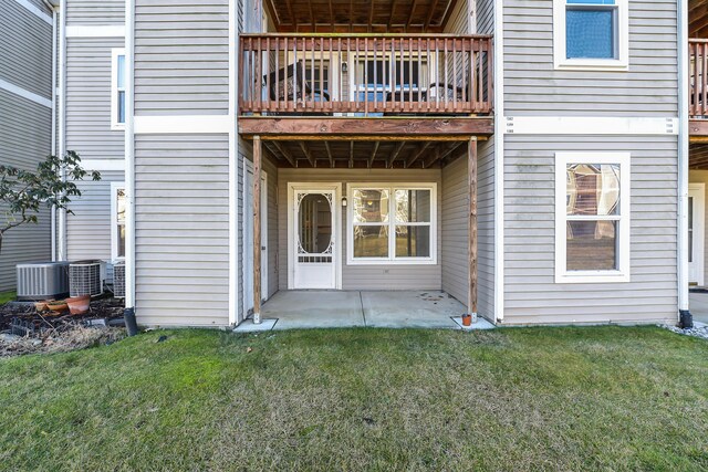 view of exterior entry featuring a lawn, a patio area, a balcony, and central AC unit