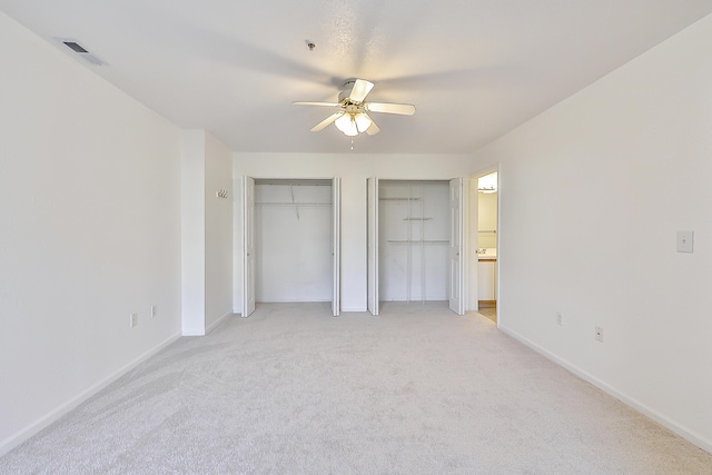 unfurnished bedroom featuring ceiling fan, light carpet, and two closets