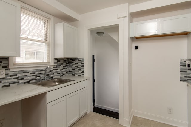 kitchen featuring sink, backsplash, white cabinetry, and light stone countertops