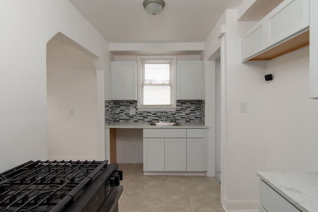 kitchen featuring light stone countertops, white cabinetry, tasteful backsplash, sink, and black gas range