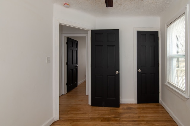 unfurnished bedroom featuring ceiling fan, light hardwood / wood-style flooring, a textured ceiling, and multiple windows