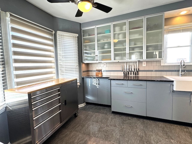 kitchen featuring backsplash, ceiling fan, sink, and dark stone counters