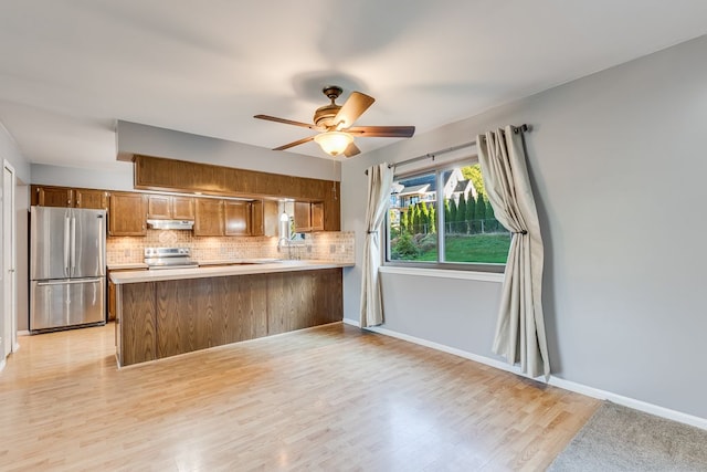 kitchen with kitchen peninsula, light wood-type flooring, backsplash, stainless steel appliances, and ceiling fan