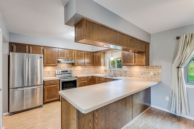 kitchen with sink, stainless steel appliances, kitchen peninsula, light hardwood / wood-style floors, and decorative backsplash