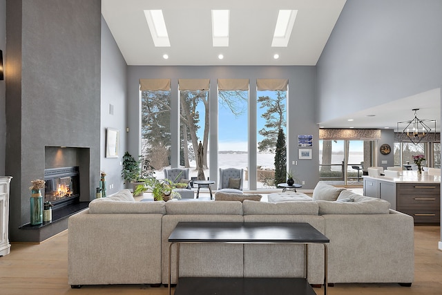 living room with a skylight, high vaulted ceiling, a water view, a notable chandelier, and light wood-type flooring