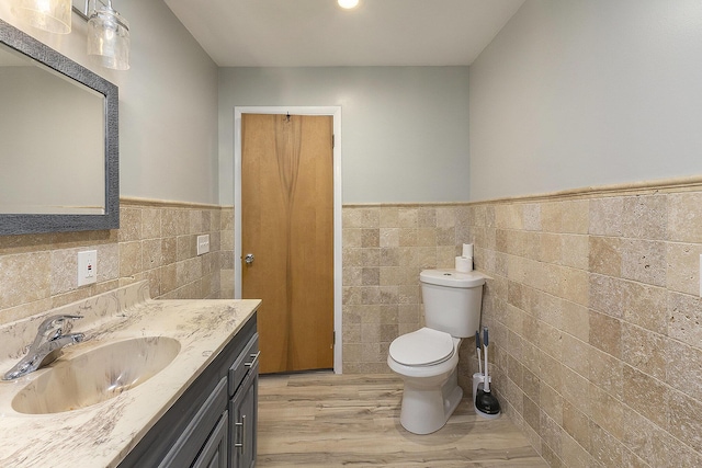 bathroom with wood-type flooring, vanity, toilet, and tile walls