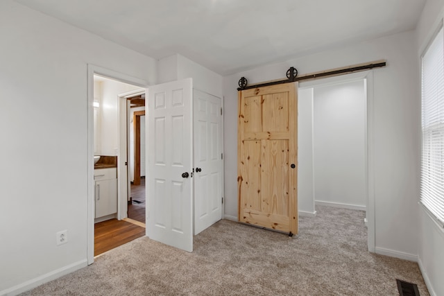 unfurnished bedroom with light carpet, a barn door, and ensuite bath