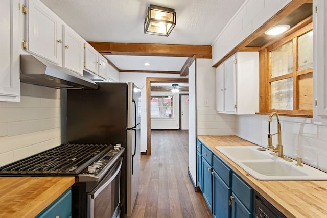 kitchen featuring butcher block countertops, under cabinet range hood, and blue cabinetry