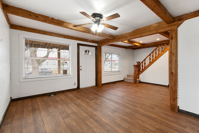 interior space featuring ceiling fan, dark hardwood / wood-style floors, beam ceiling, and brick wall