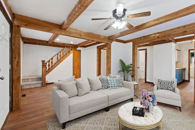 living area with ceiling fan, stairs, beamed ceiling, and wood finished floors