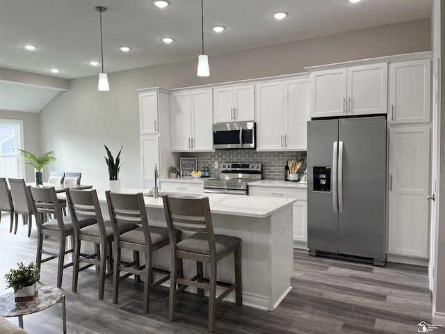 kitchen featuring appliances with stainless steel finishes, decorative light fixtures, white cabinetry, and an island with sink