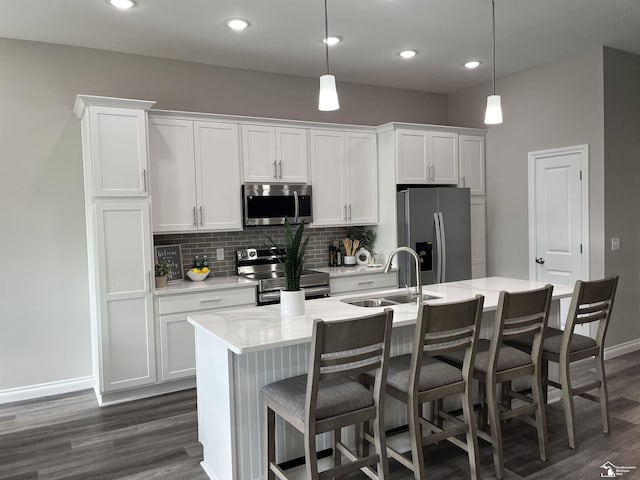 kitchen featuring white cabinets, pendant lighting, stainless steel appliances, and a center island with sink