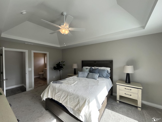 bedroom with carpet floors, a tray ceiling, ceiling fan, and ensuite bathroom