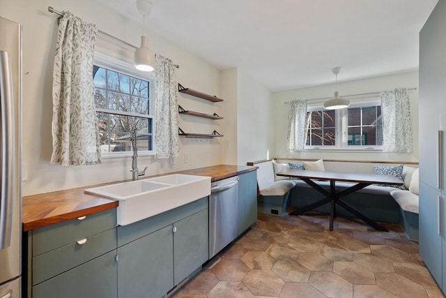 kitchen featuring wooden counters, breakfast area, sink, hanging light fixtures, and stainless steel dishwasher