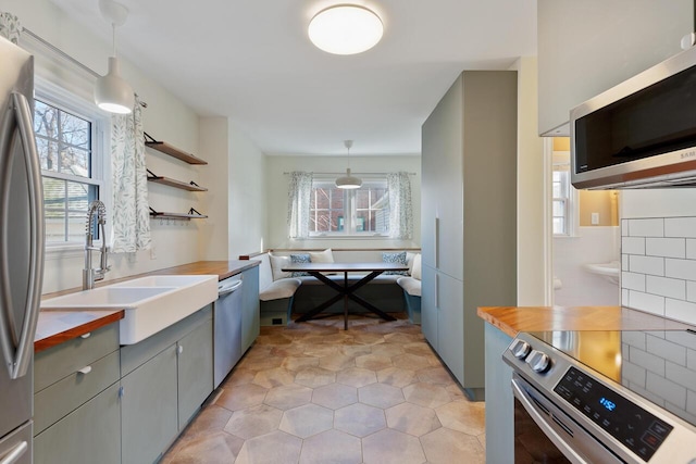 kitchen featuring butcher block counters, sink, breakfast area, decorative light fixtures, and appliances with stainless steel finishes