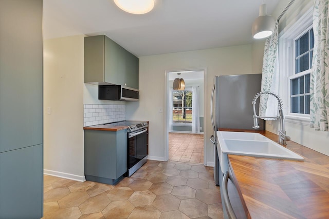 kitchen with wood counters, sink, light tile patterned floors, appliances with stainless steel finishes, and tasteful backsplash