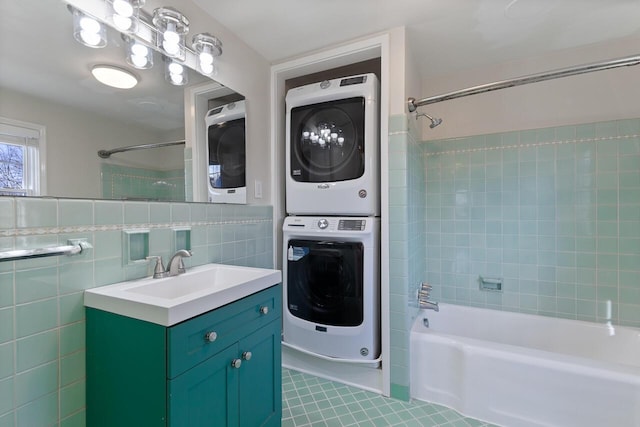 bathroom with tile patterned floors, stacked washer / drying machine, vanity, tile walls, and tiled shower / bath