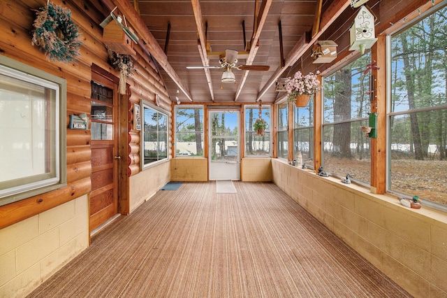 unfurnished sunroom featuring ceiling fan, beam ceiling, wooden ceiling, and a wealth of natural light