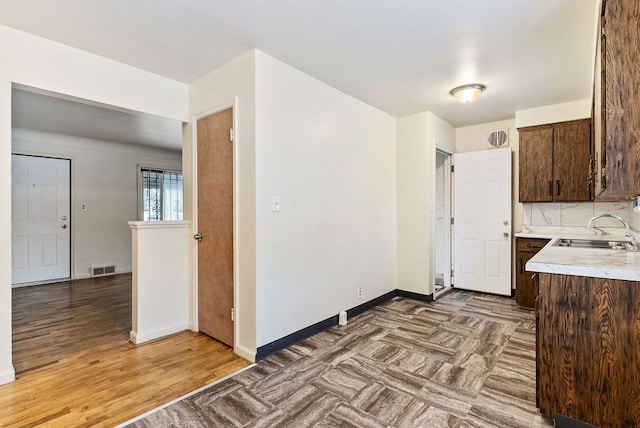 kitchen featuring dark brown cabinetry, tasteful backsplash, light hardwood / wood-style flooring, and sink