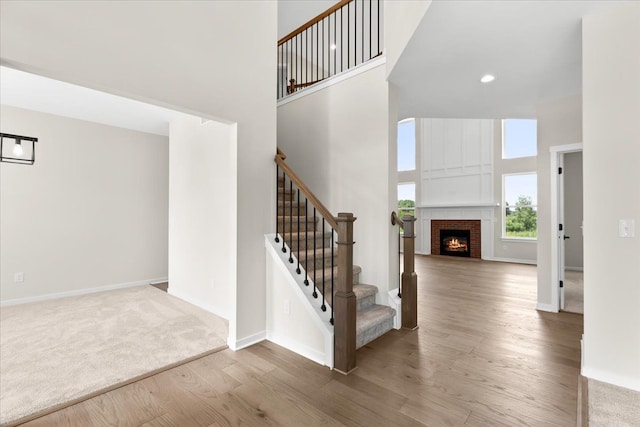 staircase with hardwood / wood-style floors, a high ceiling, and a brick fireplace