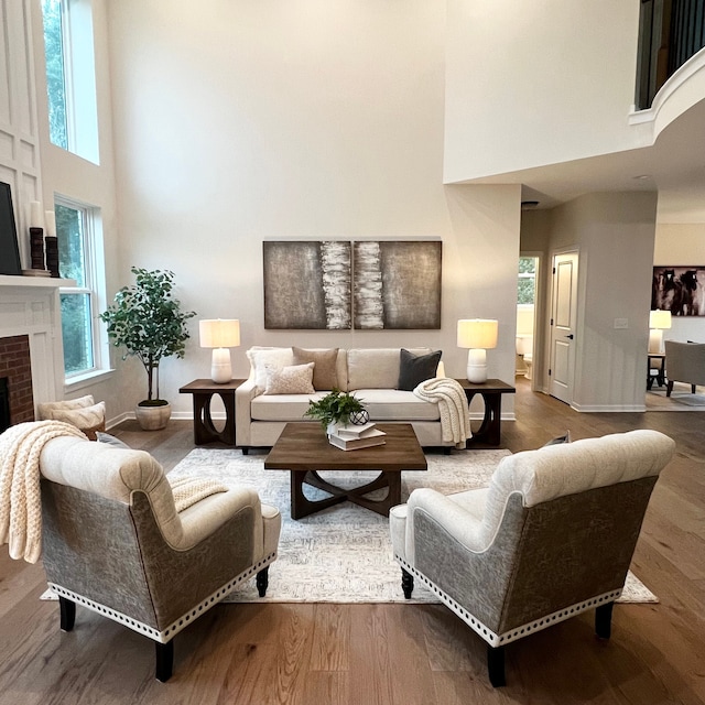 living room with a wealth of natural light, hardwood / wood-style floors, a high ceiling, and a brick fireplace