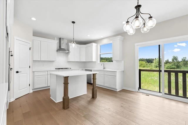 kitchen with white cabinets, wall chimney exhaust hood, a kitchen island, and hanging light fixtures