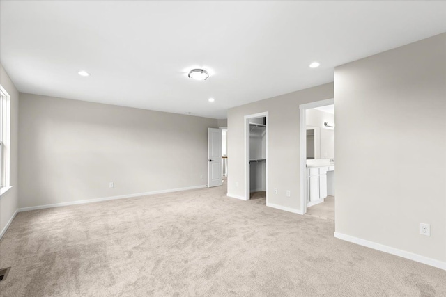 unfurnished bedroom with ensuite bathroom, a closet, a spacious closet, and light carpet