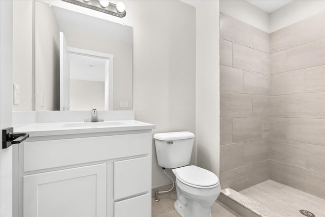 bathroom with tile patterned flooring, a tile shower, vanity, and toilet