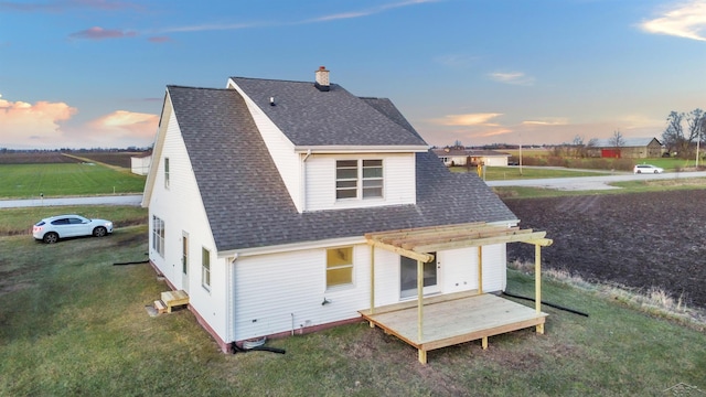 back house at dusk featuring a pergola and a lawn