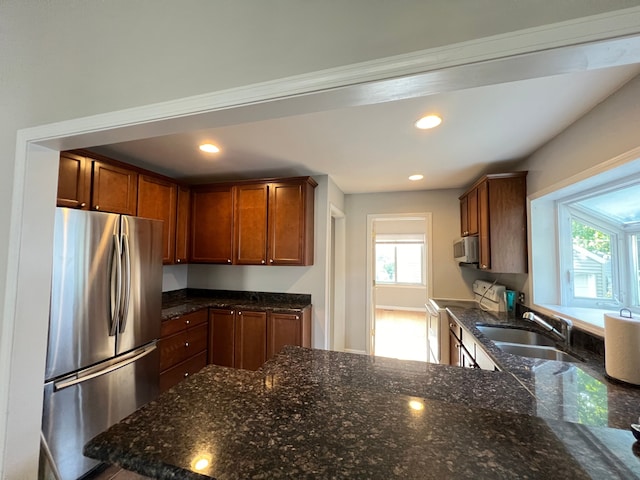 kitchen featuring kitchen peninsula, stainless steel fridge, sink, electric range, and dark stone countertops