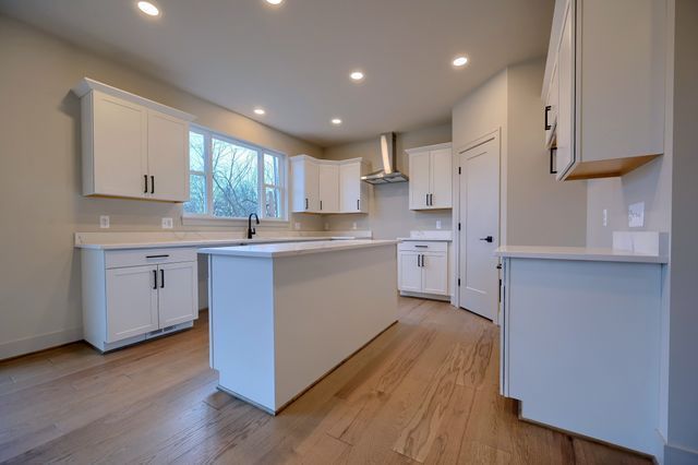 kitchen with sink, wall chimney range hood, a kitchen island, light hardwood / wood-style flooring, and white cabinets