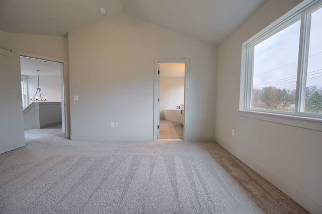 unfurnished bedroom with ensuite bath, vaulted ceiling, light colored carpet, and multiple windows