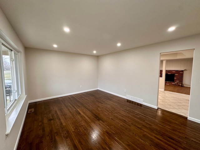 unfurnished room featuring hardwood / wood-style flooring and a brick fireplace