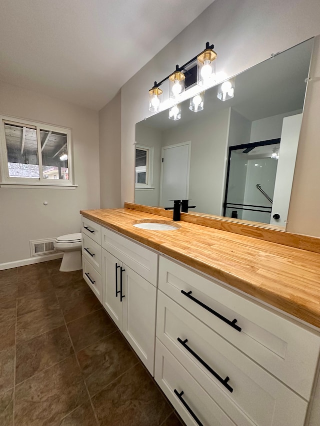 bathroom featuring a shower with door, vanity, and toilet