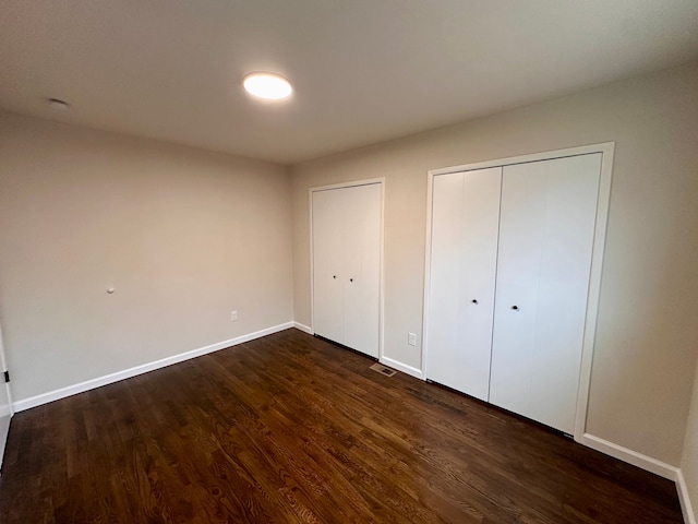 unfurnished bedroom with dark hardwood / wood-style flooring and multiple closets