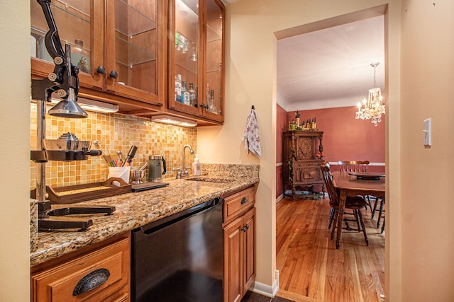 kitchen with light stone countertops, dishwasher, sink, an inviting chandelier, and backsplash